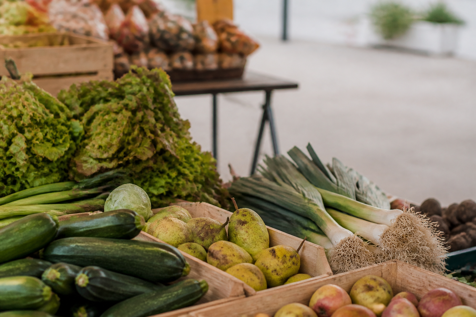 Étal de marché en fin d'été garni de cagettes de tomates de plusieurs formes, de courges, de pommes et de paniers de noix, sous une bâche de toile